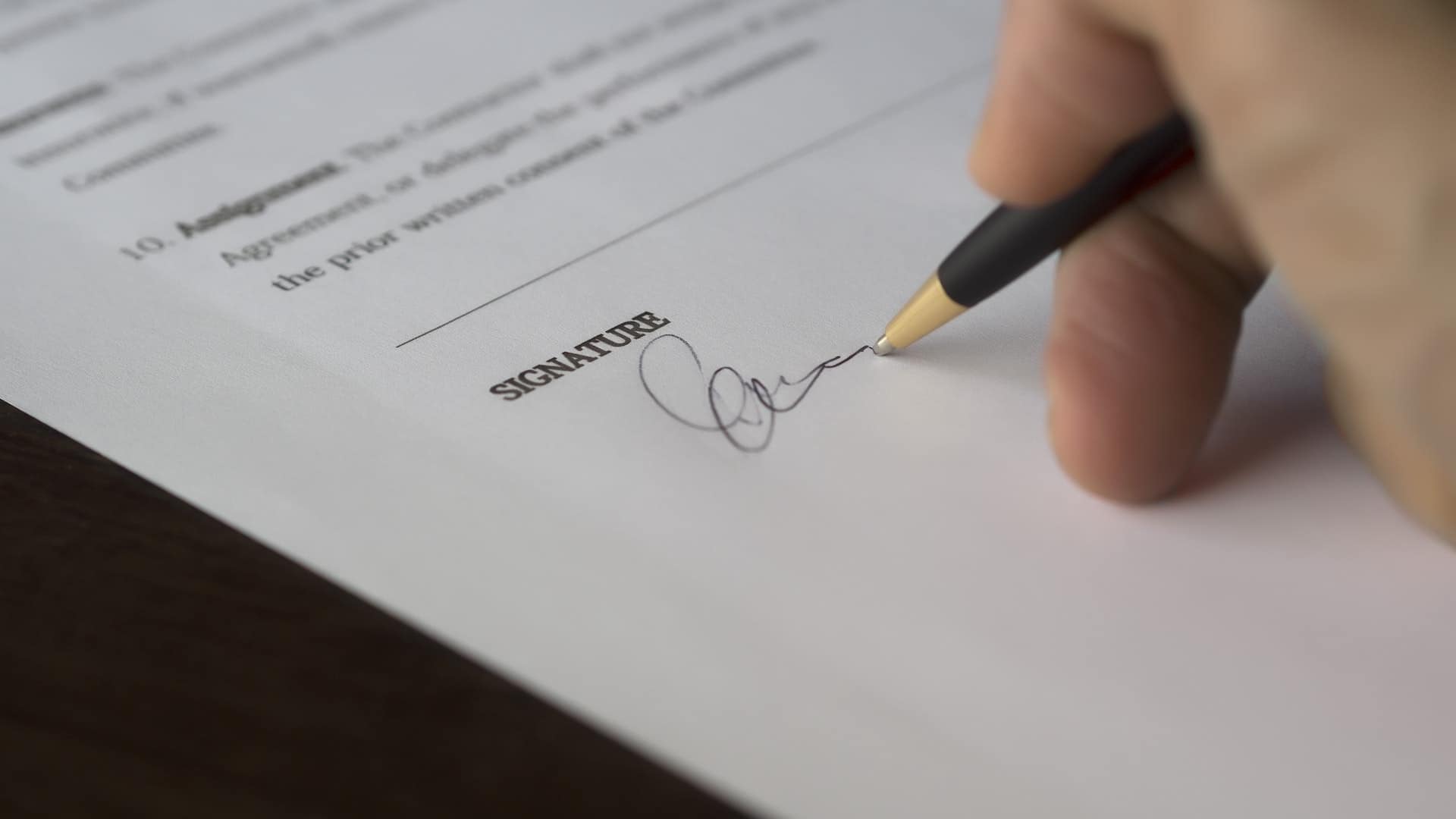 pexels-pixabay-261621 Hand holding a pen and signing a document with the word ‘SIGNATURE’ on it, symbolizing agreement or contract signing