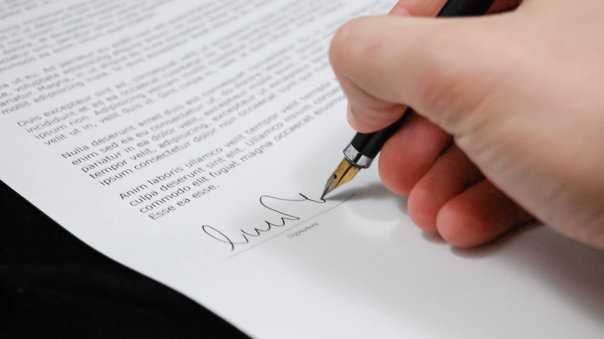 Hand signing a document with a fountain pen on a white surface